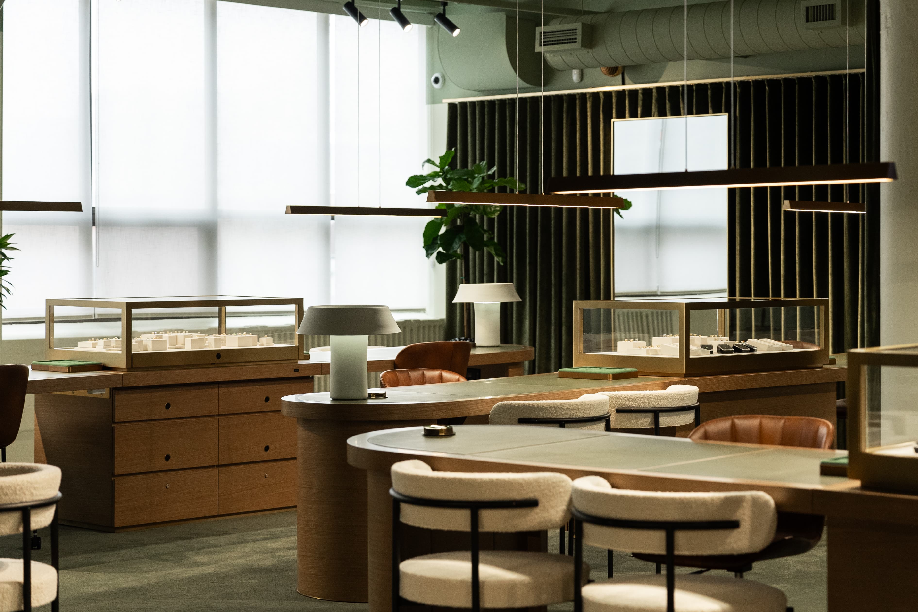 Cullen Jewellery display cases — brass-framed vitrines, custom wood casework, oval green-leather consultation table and boucle seating